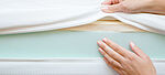 Frauenhände berühren verschiedene Schichten einer neuen Matratze. 