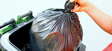 Eine Person wirft einen Müllbeutel in die Mülltonne. 